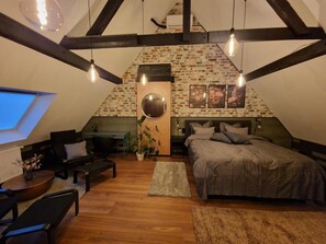 Camera mansardata con soffitto spiovente, pareti in mattoni a vista, un lucernario, un letto, una scrivania e un angolo salotto.