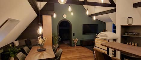 A loft-style room with a wooden dining table, chairs, and a hexagonal patterned rug.