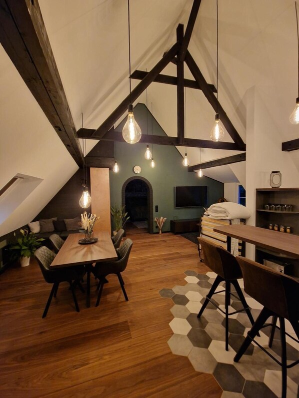 A loft-style room with a wooden dining table, chairs, and a hexagonal patterned rug.