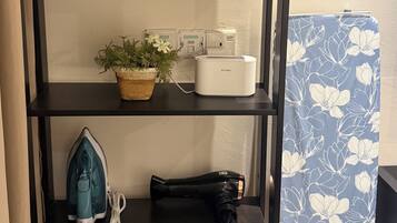 A black shelving unit with various items including a D-Link router, an iron, and a floral-patterned ironing board cover.
