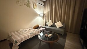 A small, cozy room with a bed, a sofa, a coffee table, and a wall-mounted air conditioner. - Keke Homestay Riverson KK Kota Kinabalu City Centre Sabah Imago Shopping Mall (Kota Kinabalu)