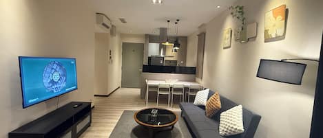 A modern living room with a flat-screen TV, a sofa, a coffee table, and a dining area with chairs.