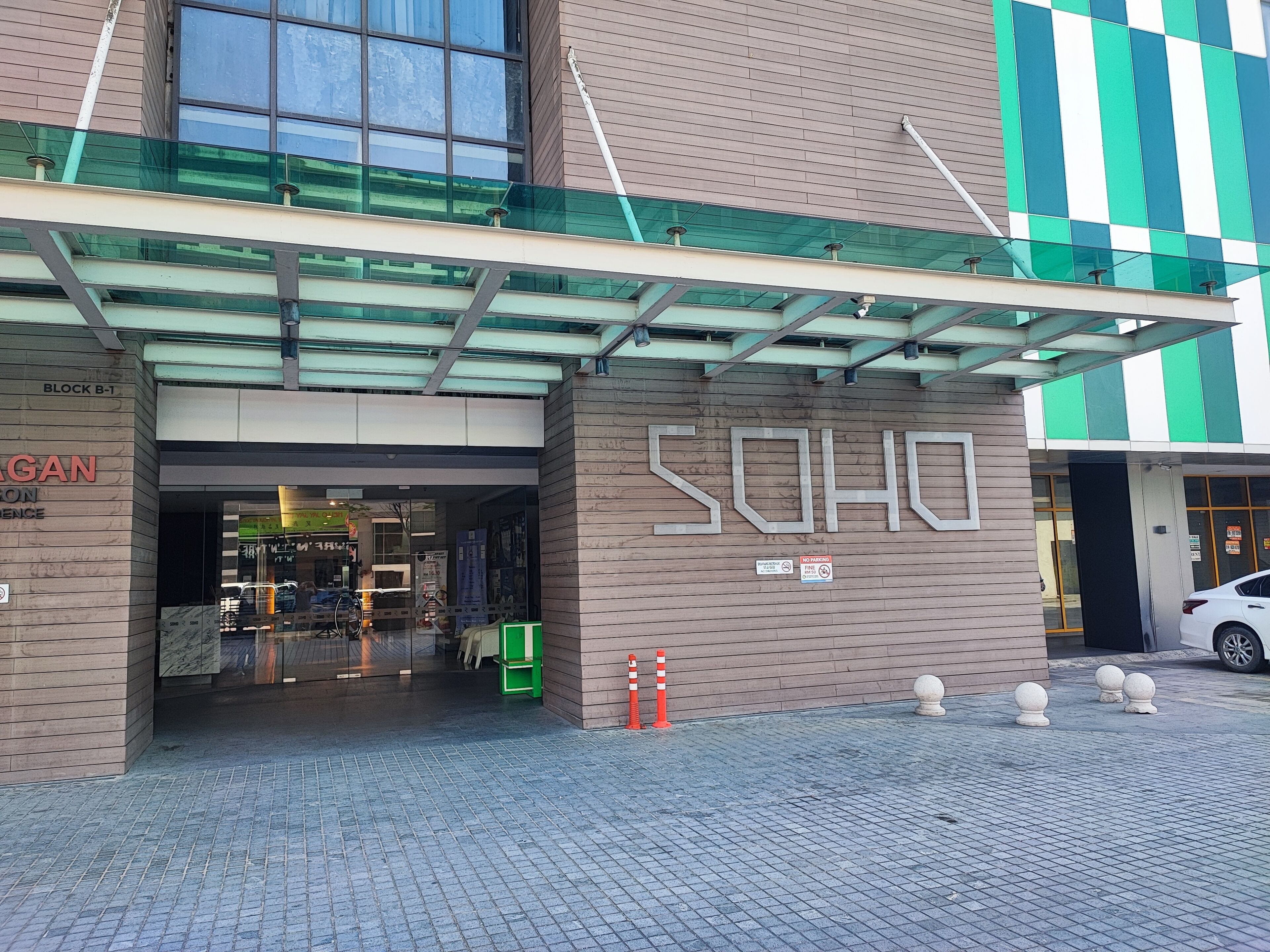 A building entrance with a glass canopy, a sign reading 'SOHO', and a parking sign indicating no parking.