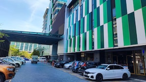 Un bâtiment moderne à la façade verte et blanche, doté d’une allée couverte et d’un parking où sont stationnées différentes voitures.