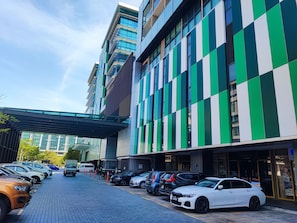 Een modern gebouw met een geel-wit gevel, een overdekte gang en een parkeerplaats met diverse auto's.
