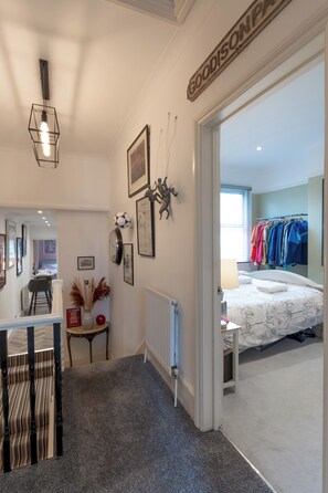 Une chambre d’hôtel comprenant un lit, une armoire, un bureau avec une chaise, un radiateur et un mur orné de tableaux et d’une enseigne.