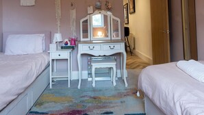 Quarto com duas camas, penteadeira, espelho e luminária pendente.