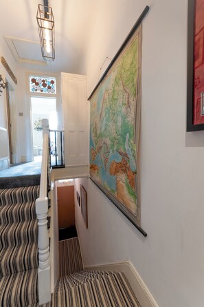Un escalier recouvert d’une moquette à rayures mène à un palier où une grande carte est accrochée au mur.