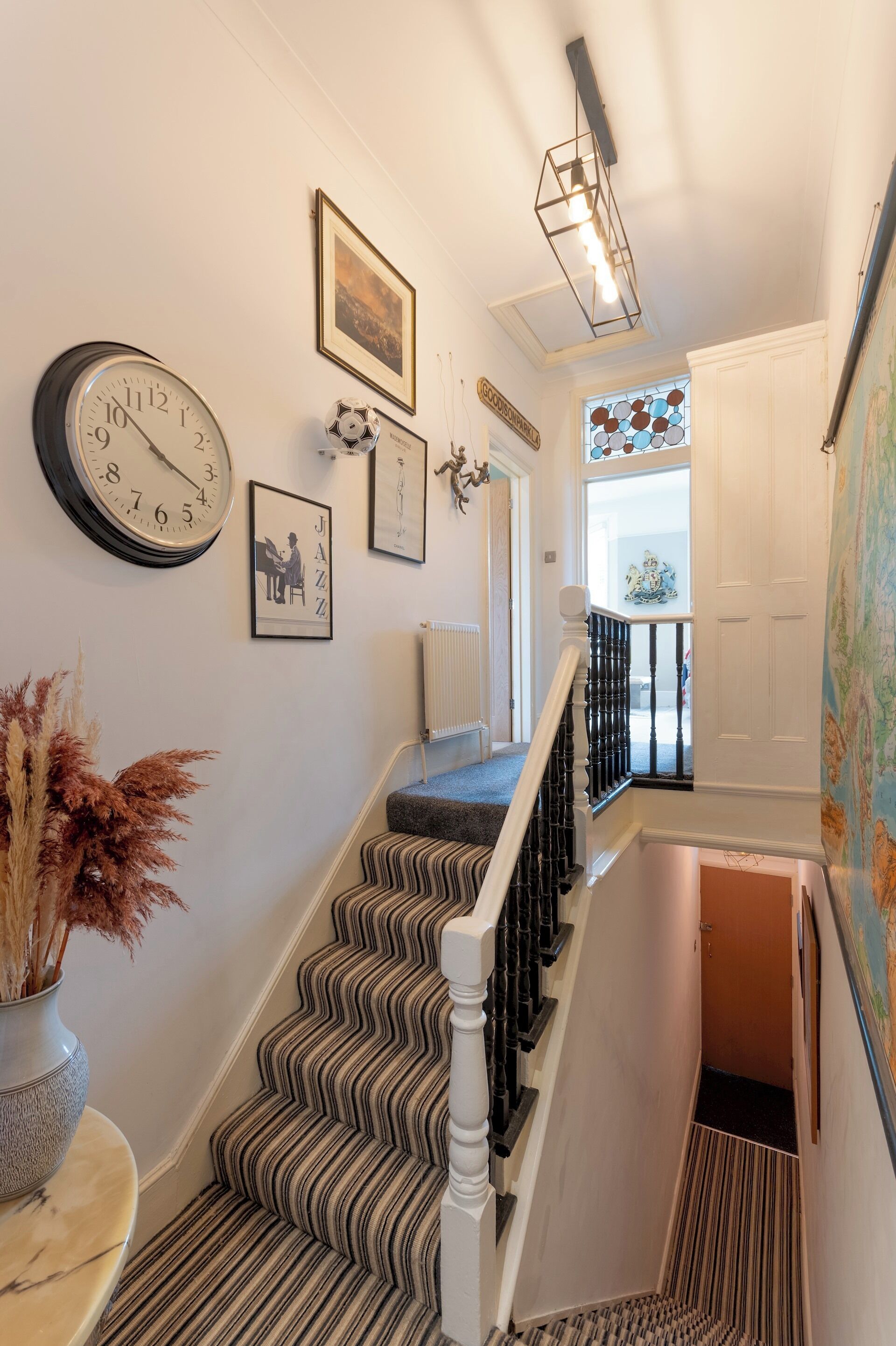 A staircase with a patterned carpet, a wall clock, and framed artwork.