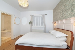 Un dormitorio con cama, ventana con cortinas, radiador, pared con papel tapiz estampado y lámpara colgante.