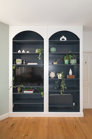 Ein Zimmer mit einer schwarzen, bogenförmigen Regaleinheit an einer weißen Wand, mit verschiedenen Dekorationsgegenständen und einem Fernseher.