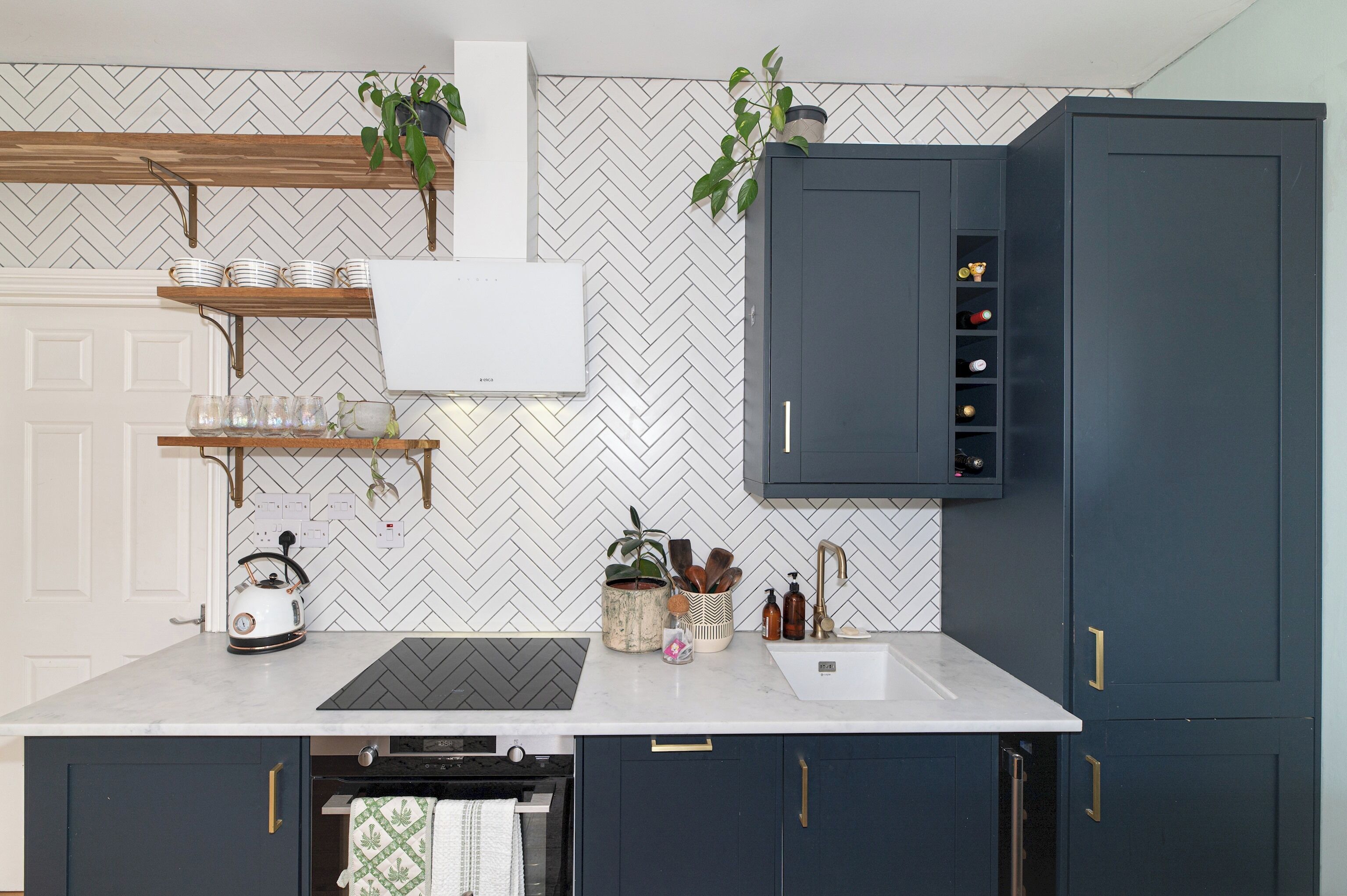 A modern kitchen with a white countertop, dark cabinets, and a herringbone-patterned backsplash.