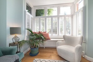 Une pièce avec une baie vitrée, un canapé, un fauteuil, une lampe et une plante en pot.