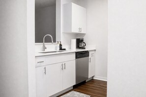 A modern kitchen with white cabinetry, a stainless steel dishwasher, and a coffee maker. - Spacious 4-bedroom apartment with AC in beautiful Gainesville. (Gainesville)