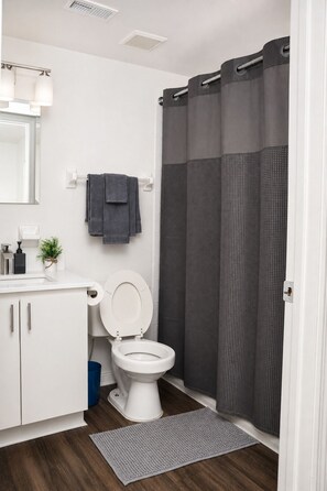A bathroom with a toilet, a sink, a mirror, a towel rack, and a shower curtain. - Spacious 4-bedroom apartment with AC in beautiful Gainesville. (Gainesville)