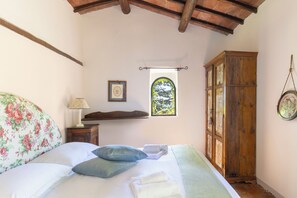 Une chambre à coucher comprenant un lit, des oreillers, une table de chevet, une lampe, une fenêtre donnant sur un beau paysage et une armoire en bois.