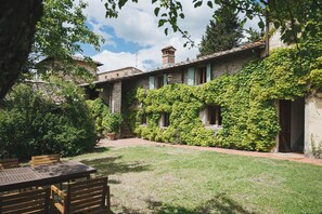 Une cour avec un bâtiment en pierre, une table en bois et des chaises.
