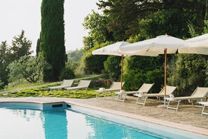 Un espace aménagé au bord de la piscine, avec des chaises longues et des parasols, le tout entouré de verdure.