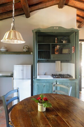 Cozinha com mesa de madeira, cadeiras, luminária pendente e armário verde com utensílios de cozinha.