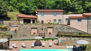 Edificio de dos pisos con piscina, paredes de piedra y área de estar al aire libre.