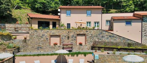 Edificio de dos pisos con piscina, paredes de piedra y área de estar al aire libre.