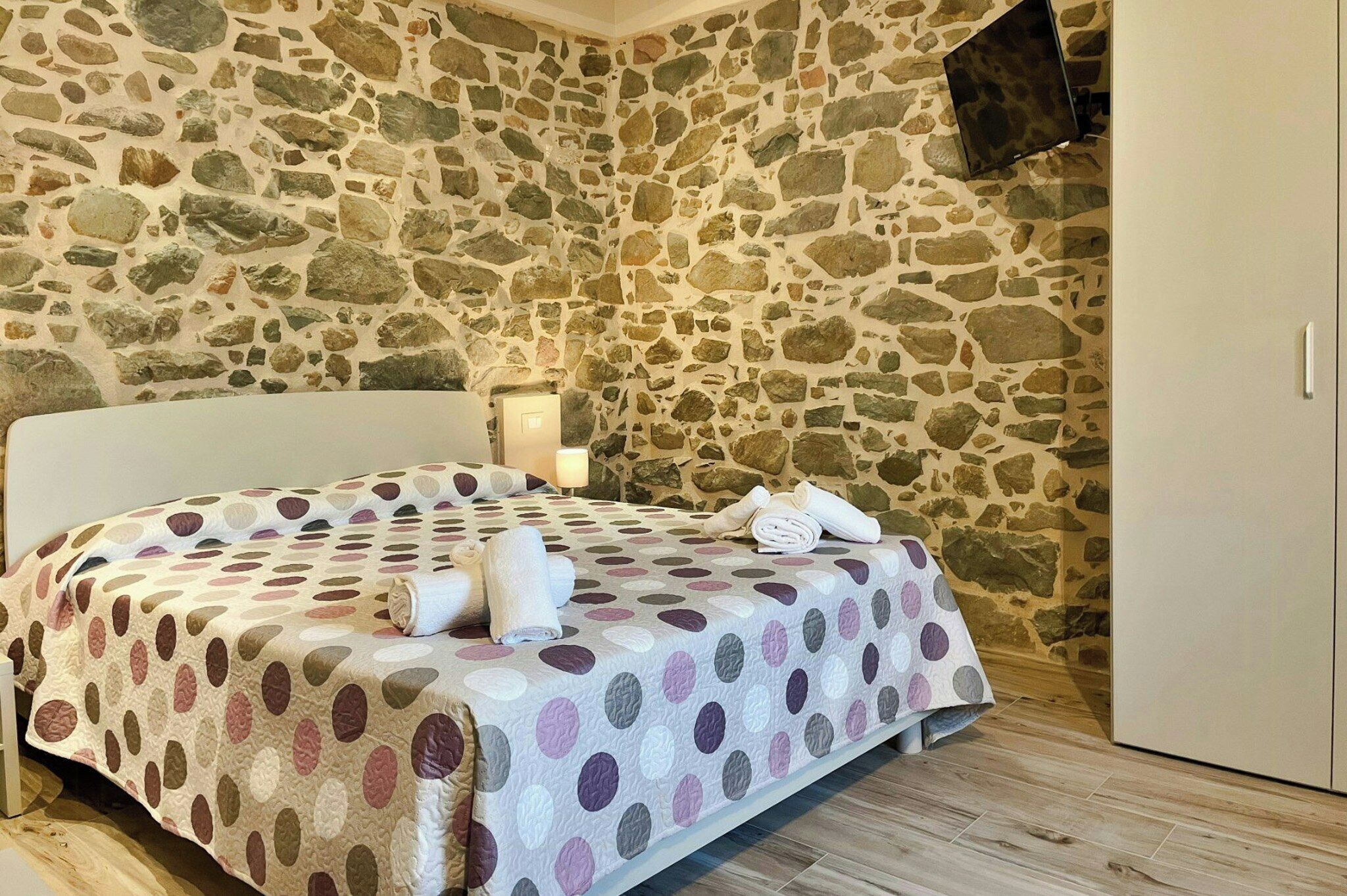Une chambre avec un mur en pierre, un lit recouvert d’une couvre-lit à pois et une armoire blanche.
