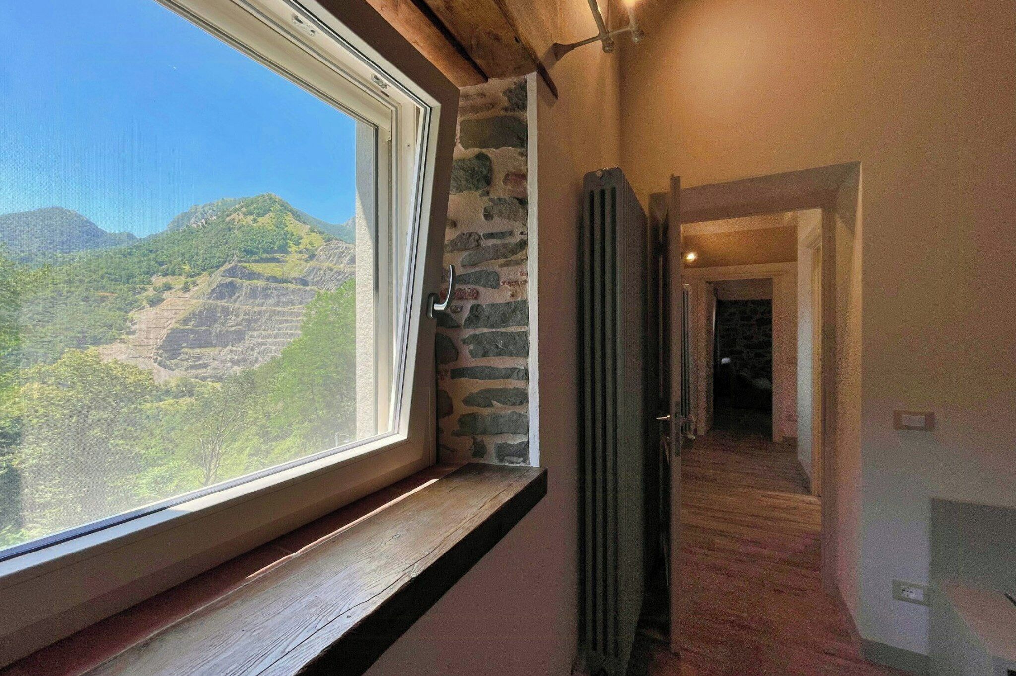 A corridor with a view of mountains through a window, a stone wall, and a wooden door.