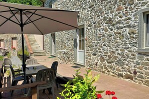 Ein Steinhaus mit Terrasse, Mobiliar und einem Tisch mit Sonnenschirm.