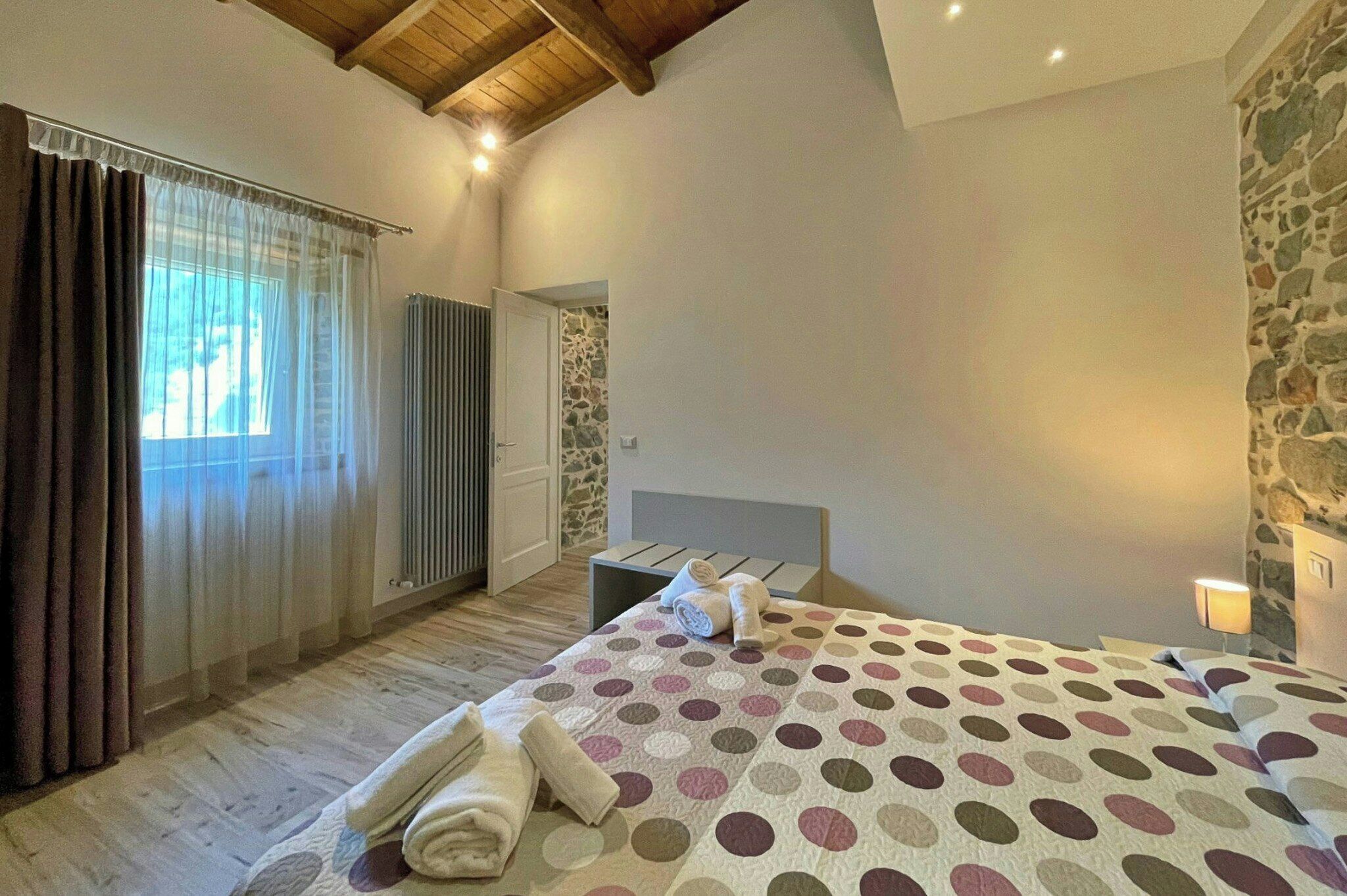 Un dormitorio con cama, radiador, pared de piedra y ventana con cortinas.