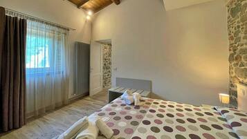 Un dormitorio con cama, radiador, pared de piedra y ventana con cortinas.