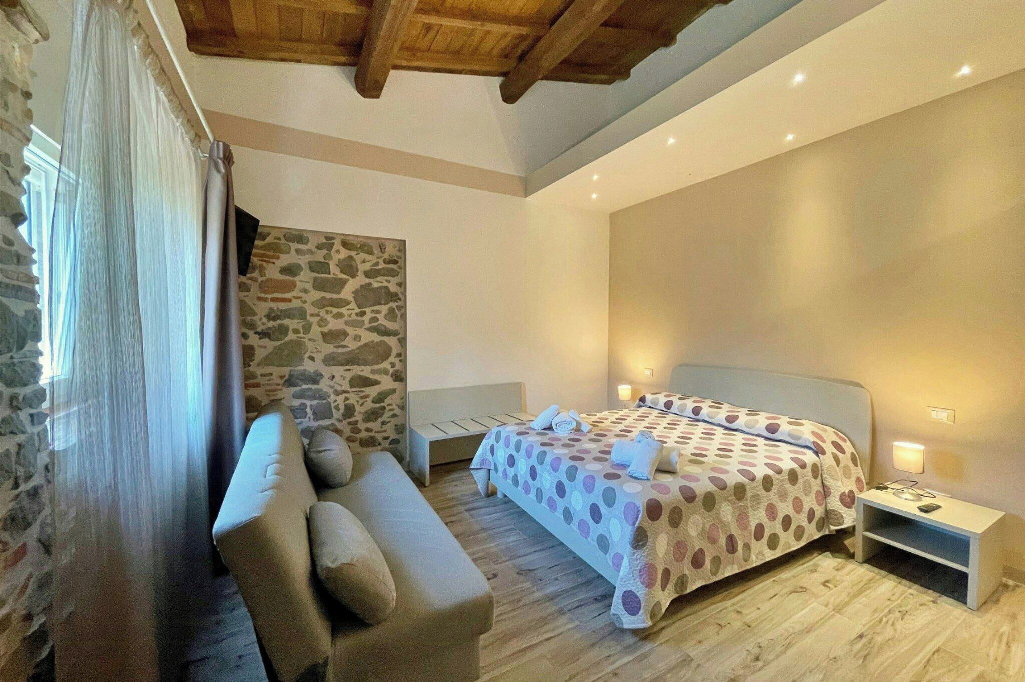 Una camera da letto con un letto, un comodino, un divano e un muro in pietra.