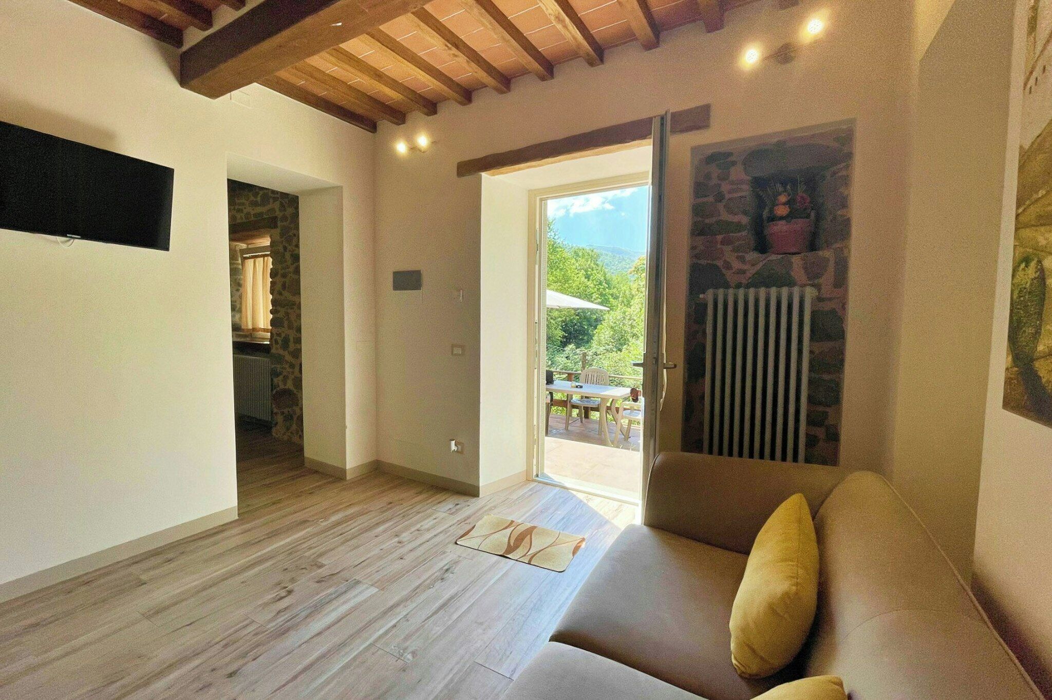A room with a wooden floor, a sofa with cushions, a stone wall, and a view through a glass door.