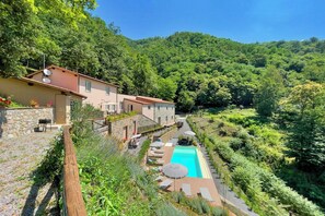 Eine Villa an einem Hang mit Swimmingpool, Sitzgelegenheiten im Freien und üppiger Bepflanzung.