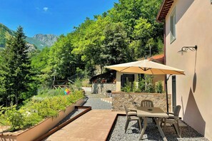 Un patio con una mesa, sillas, un paraguas grande y un muro de piedra.
