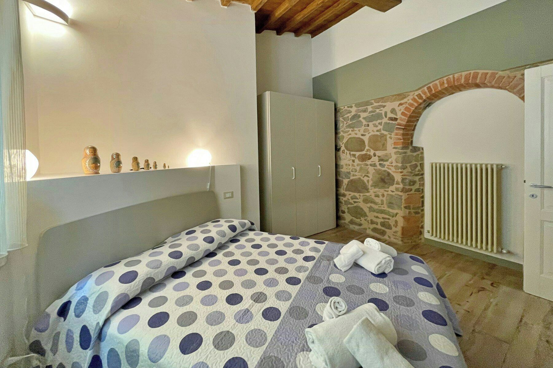 Une chambre à coucher avec un lit, une armoire, un radiateur et un mur en pierre.