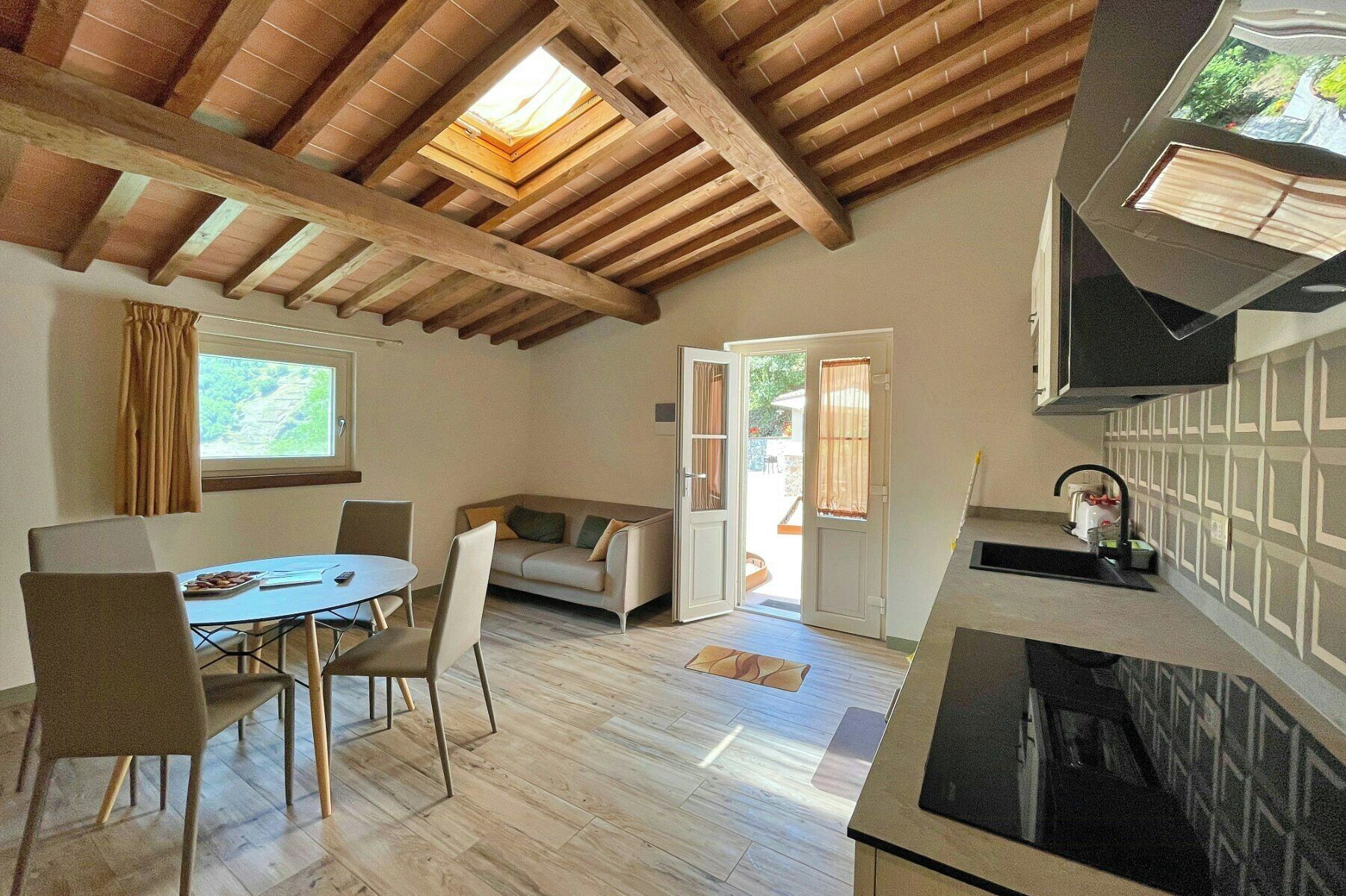 A modern kitchen with a wooden ceiling, a dining area with a table and chairs, and a view through an open door to an outdoor area.