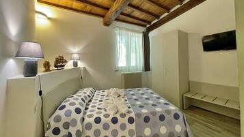 A bedroom with a bed, a nightstand, a lamp, a ship model, a window with curtains, and a TV on the wall.
