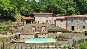 Una vila amb piscina, parets de pedra i vistes a un turó boscós.