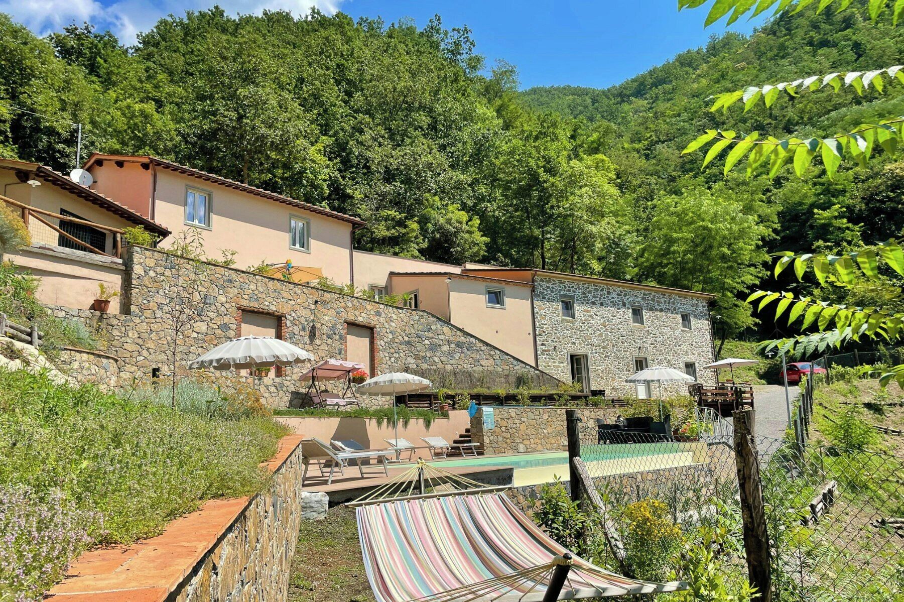 Un edificio de piedra con piscina, mobiliario de exterior y una hamaca.