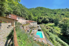 Una propiedad en una ladera con piscina, mobiliario exterior y un muro de piedra.