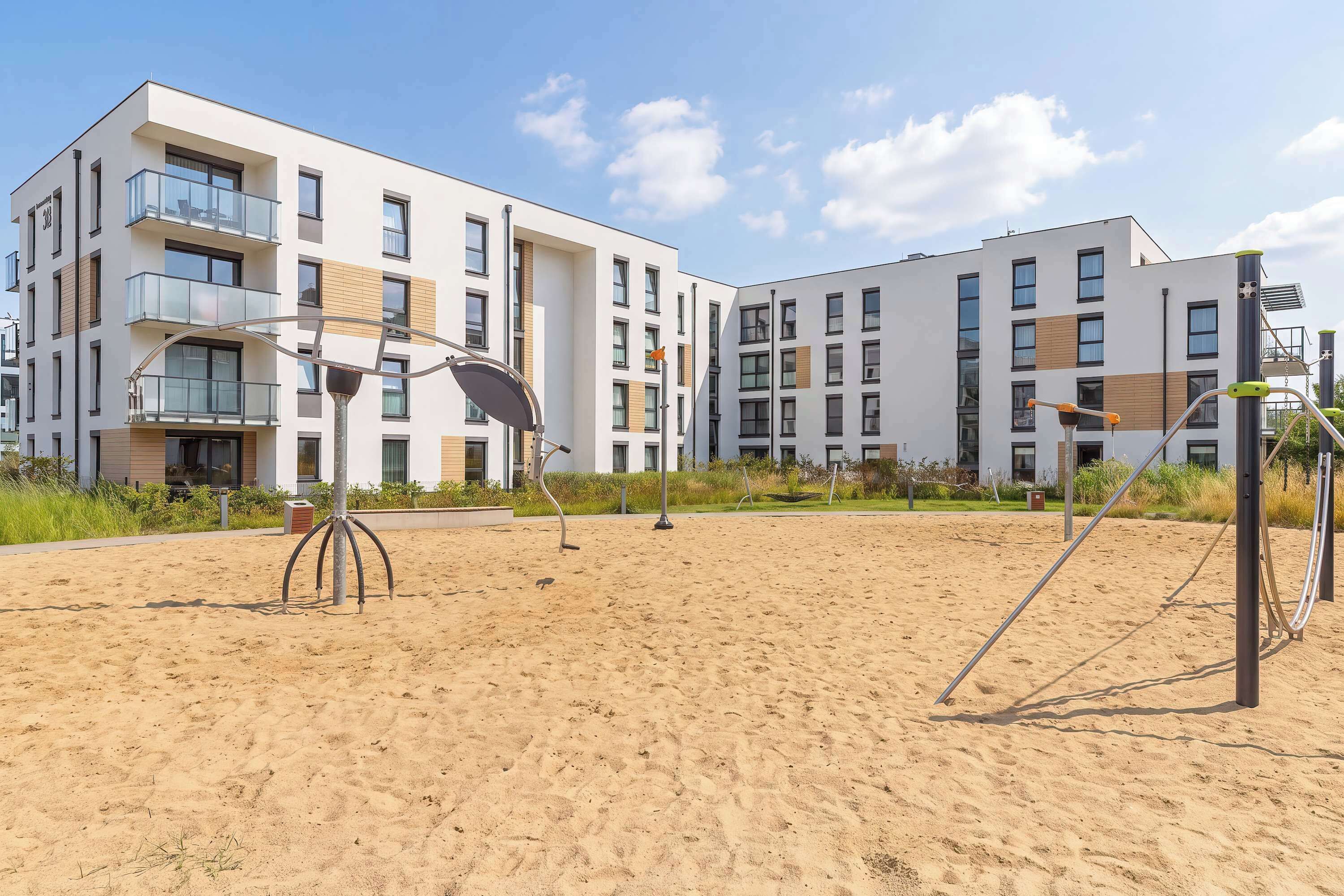 Un edificio de apartamentos moderno con varios balcones y una zona de playa arenosa con equipo de ejercicio.