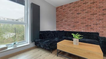 Un soggiorno moderno con un divano angolare nero, un tavolino in legno e una parete decorata con mattoni.