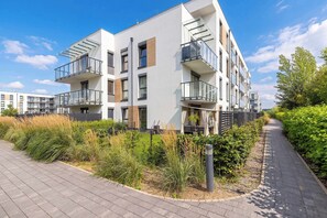 A modern multi-story residential building with balconies, a paved walkway, and surrounding greenery. - Spacious Apartment with Garden | 2 Bedrooms | Parking (Pogórze)
