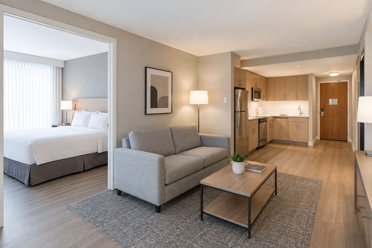 Ein Hotelzimmer mit Bett, einer Couch, einem Couchtisch, einer Küchenzeile und einer Tür zu einem weiteren Raum.