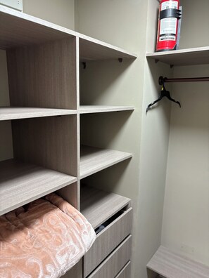 A closet with open shelves, a hanging rod, and a fire extinguisher on the top shelf.
