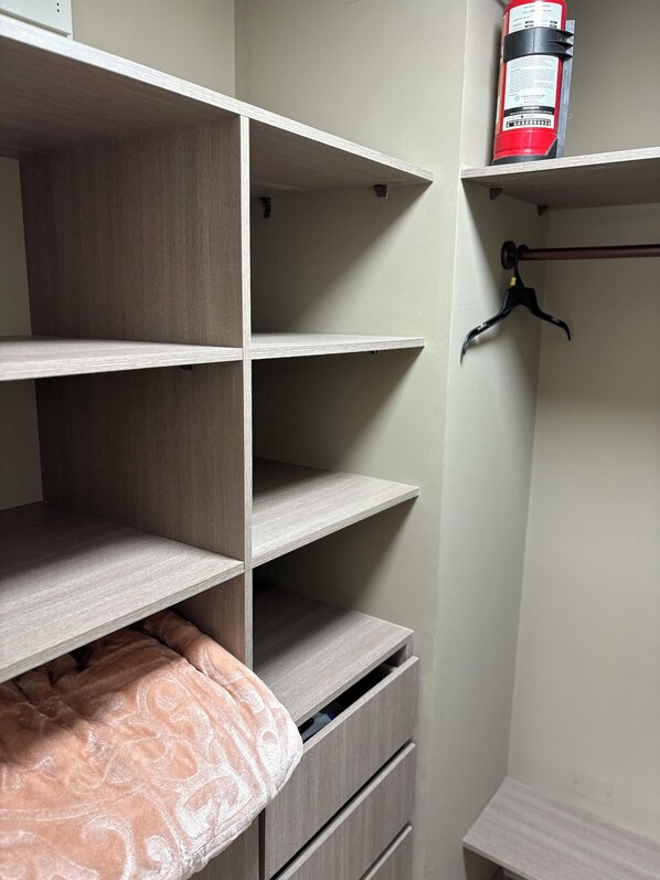 A closet with open shelves, a hanging rod, and a fire extinguisher on the top shelf.