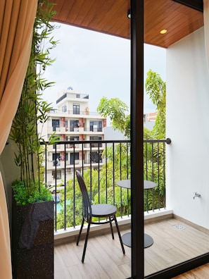 Un balcón con una silla y una mesa, vista de edificios y una planta en maceta.