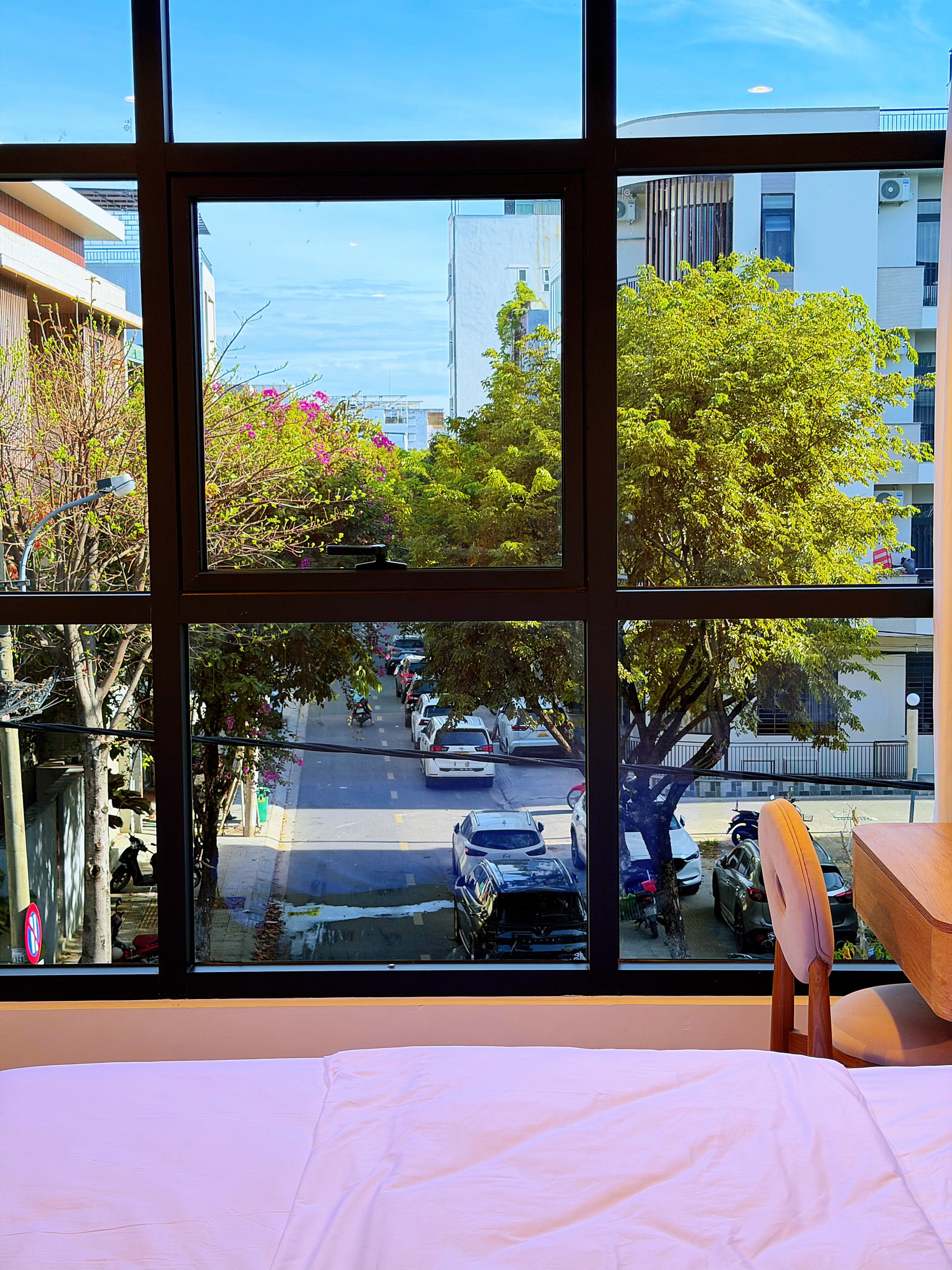 Una habitación con un amplio ventanal que da a una calle con coches aparcados y árboles.