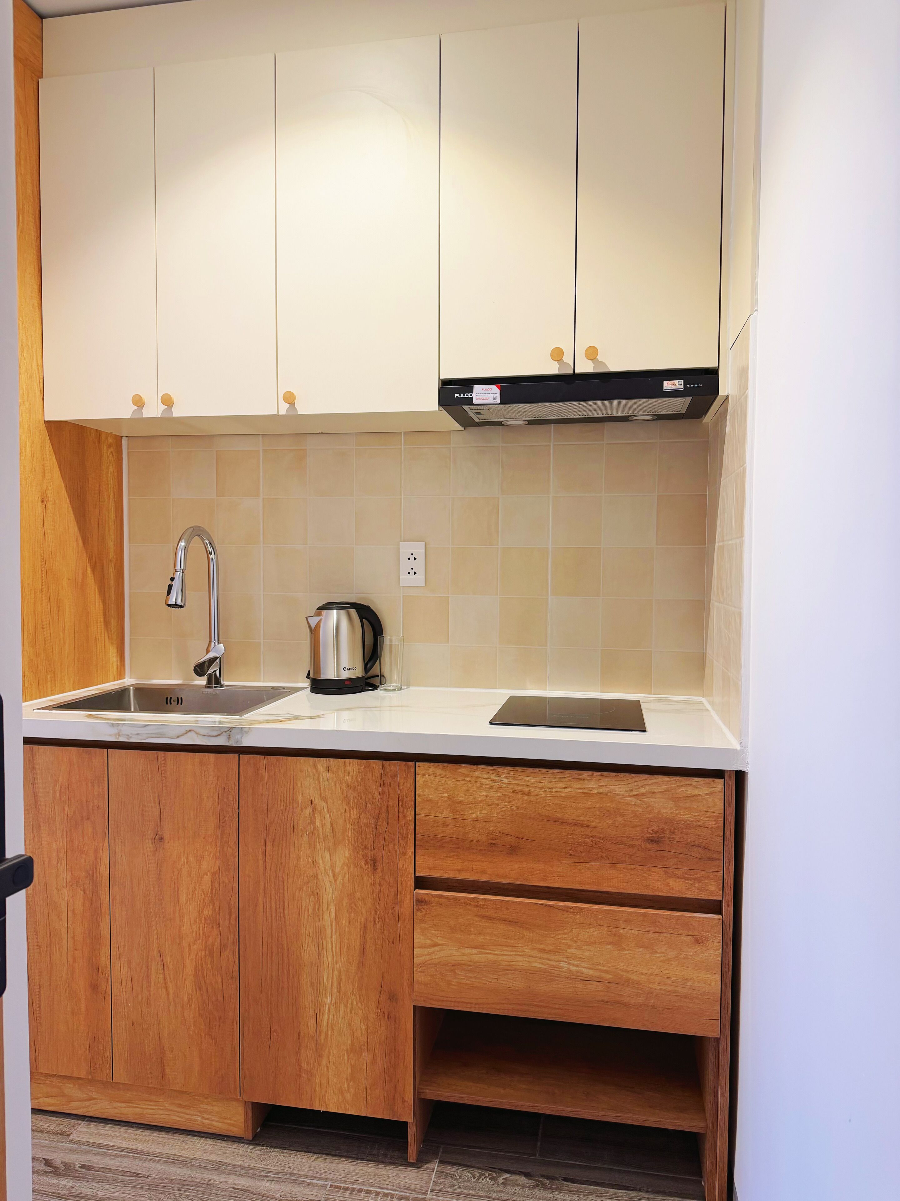 Una cocina compacta con un lavamanos, una tetera y armarios de madera.