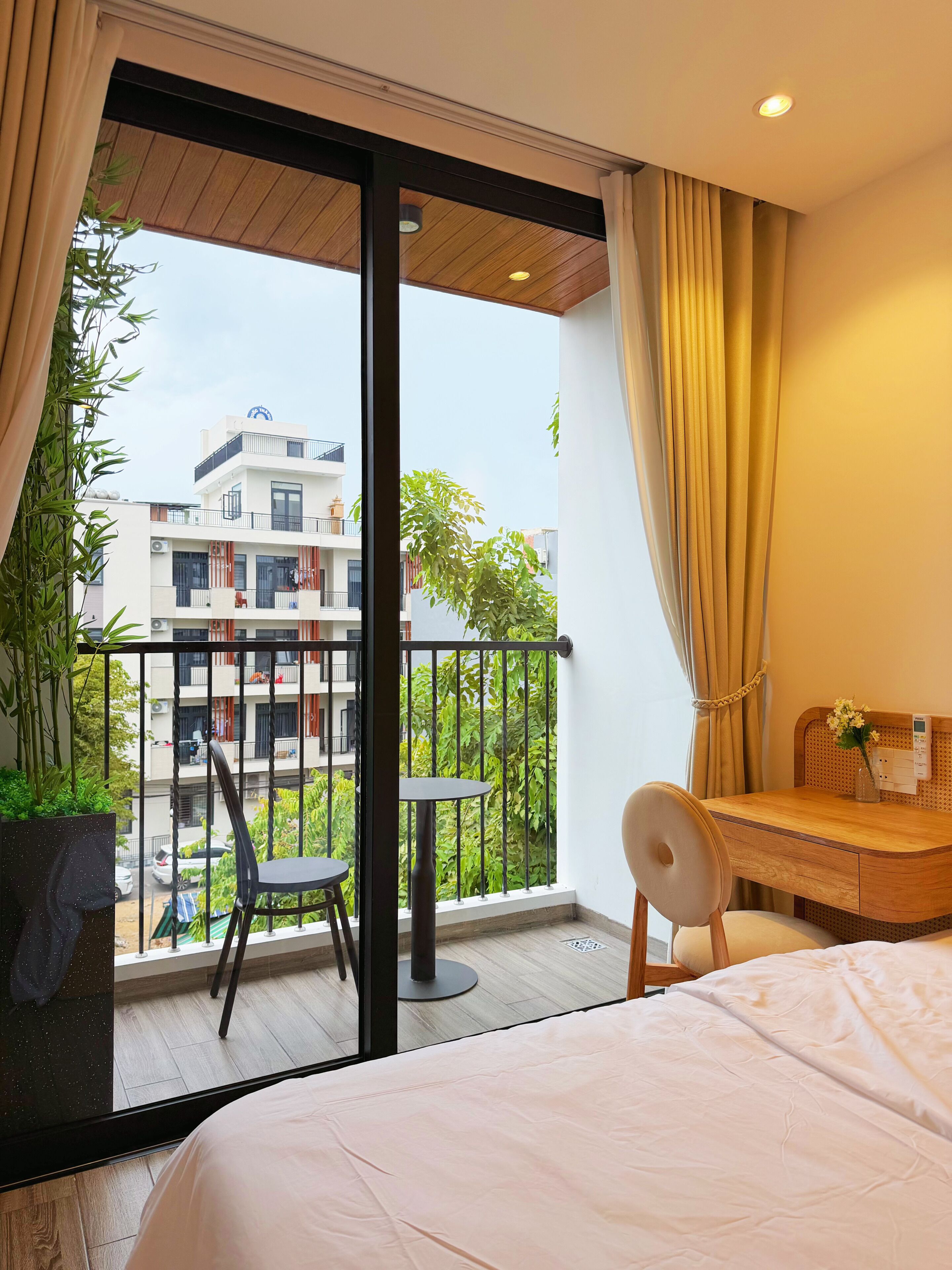 A hotel room with a bed, a desk, a chair, and a balcony with a view of the city.